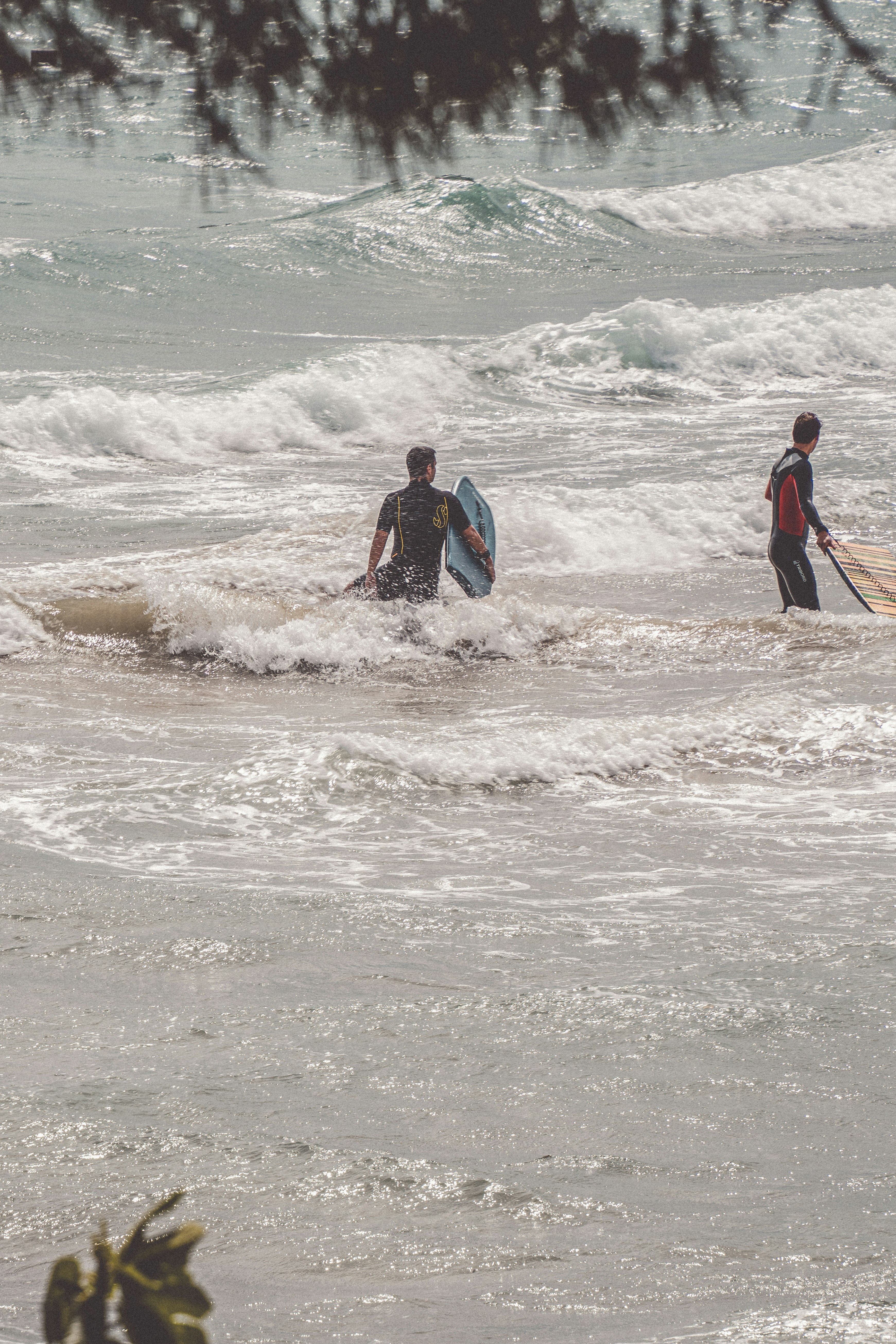 man in blue and black jacket carrying brown surfboard on beach during daytime